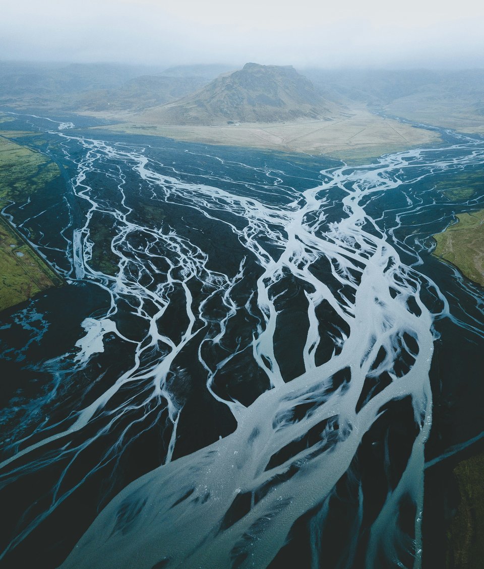 An aerial photograph of a large river, with many small tributaries, splitting in the distance around a foggy mountain.