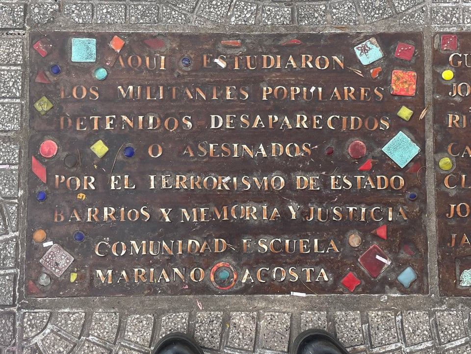 A large mosiac like brick in the sidewalk dedicated to people who were taken and disappeared by the Argentine government. “Aqui estudiaron los militantes populares detenidos-desaparecidos o asesinados por el terrorismo de estado. Barrios por Memoria y Justicia. Comunidad Escuela Mariano Acosta”  “This is where the popular activists who were detained, disappeared, or murdered by state terrorism studied. Neighborhoods for Memory and Justice. Mariano Acosta Community School.”