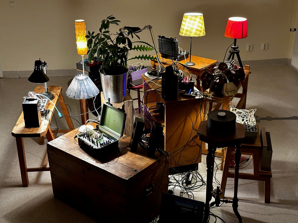 A collection of synthesizers sitting on tables and stools, lit by table lamps