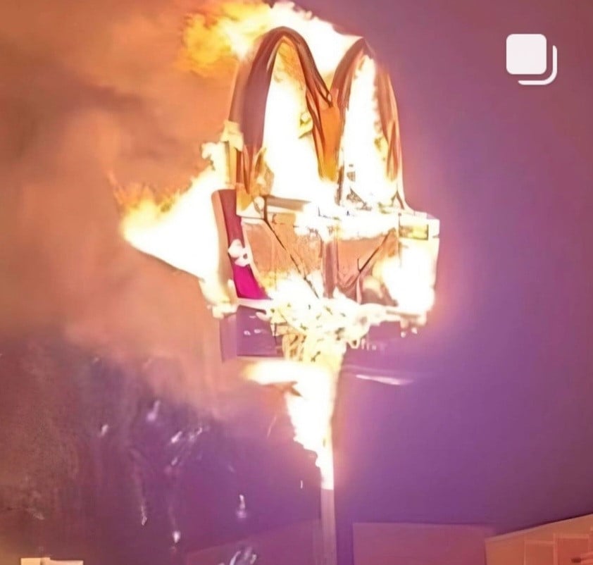 A McDonald's restaurant sign - aka the Golden Arches - fully engulged in flames, the plastic fronting that would displat the name having cracked/melted away, showing the metal frame beneath. I'm lovin' it.