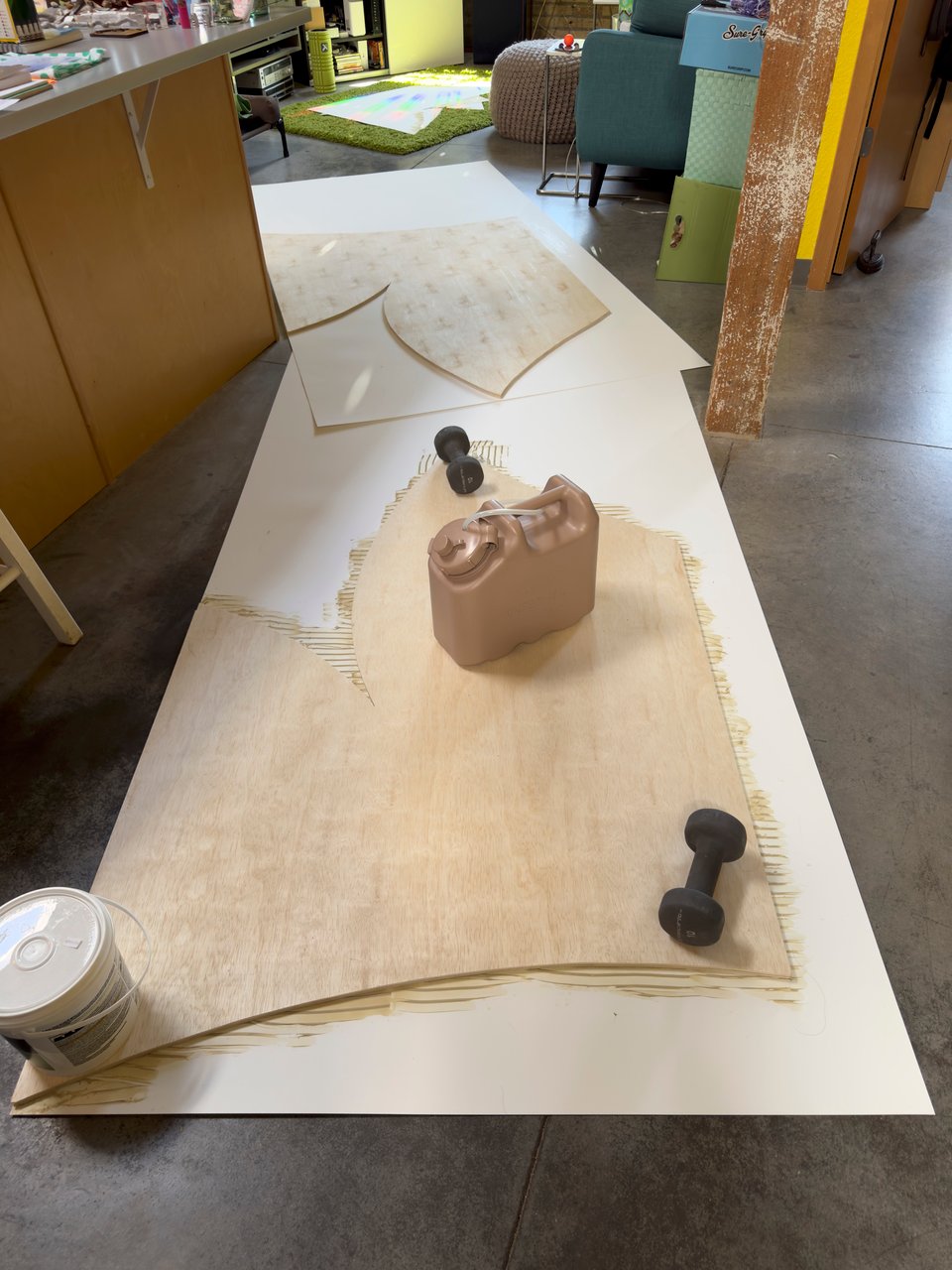 Wood pieces laying on white plastic being weighed down with hand weights, a bucket, and a water jug.