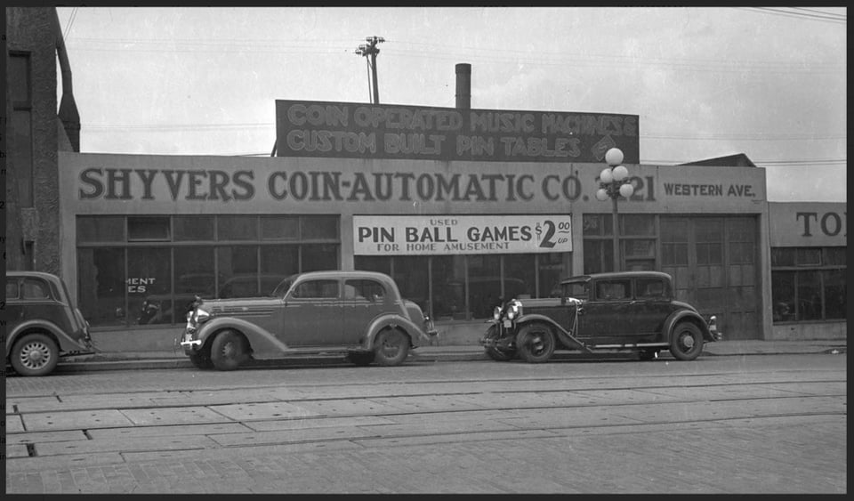 Black and white image of a street view in the 1930s in Seattle, featuring three cars and a company building named "Shyvers Coin-Automatic Co."
