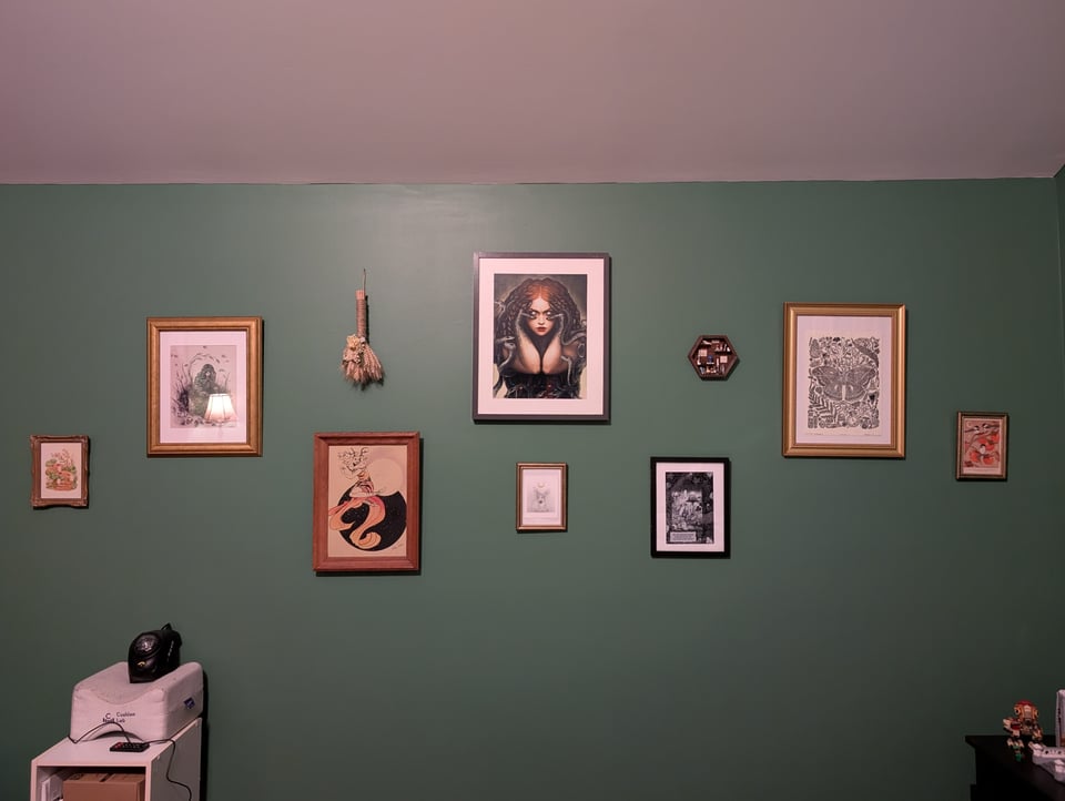 A green wall with assorted art hung on it.