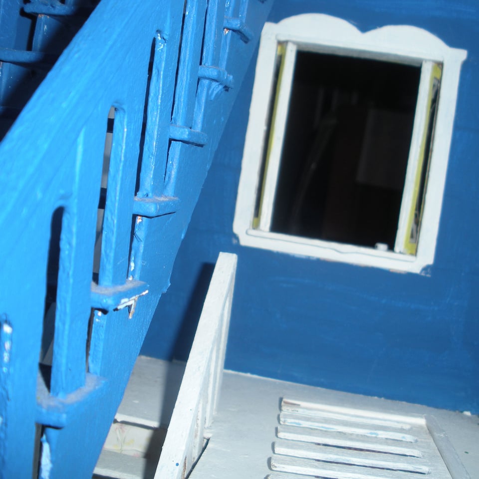 A blue staircase inside of a dollhouse. Window to darkness.