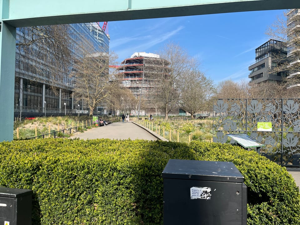 A photo of a green space in London, with plants and bushes surrounded by walkways and urban infrastructure.