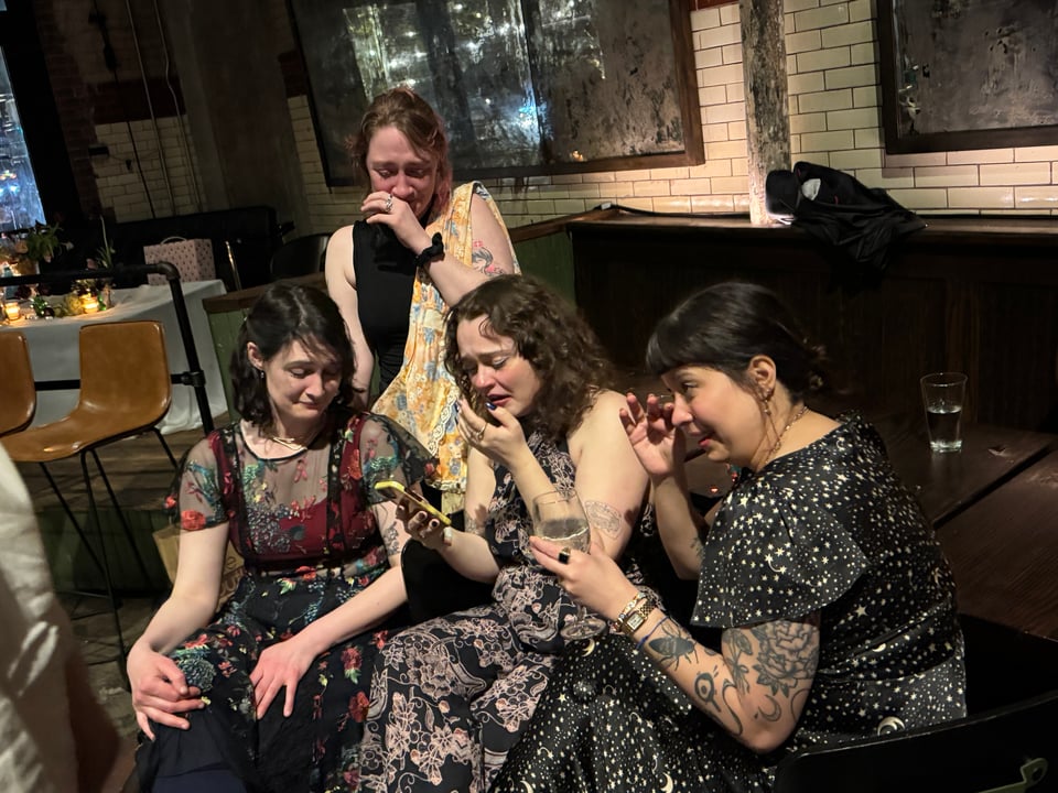 Em, Erin, Callie and Andrea, decked out in wedding fits, sobbing while reading Brendon Bigley's vows on Em's phone.