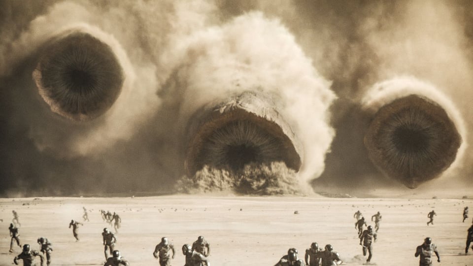 A group of people in a desert running from three massive sandowoms in Dune Part II
