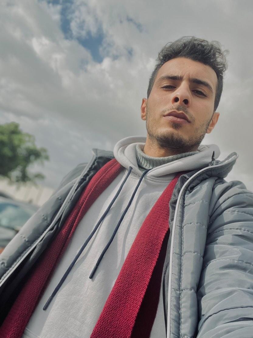 Selfie of Ahmad Johar, a young Palestinian man in a grey coat and red scarf.