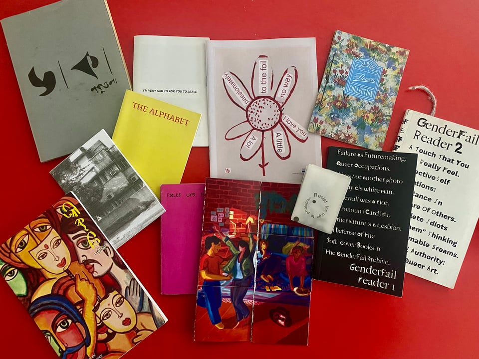 An arrangement of zines of various colours, patterns, texts, and illustrations on a red table.