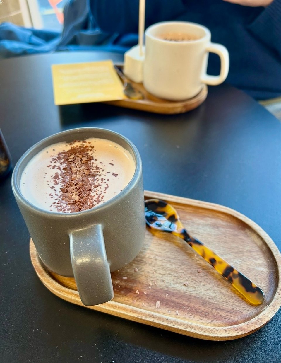 Mugs of fancy hot chocolate on small wooden trays with tortoiseshell spoons.