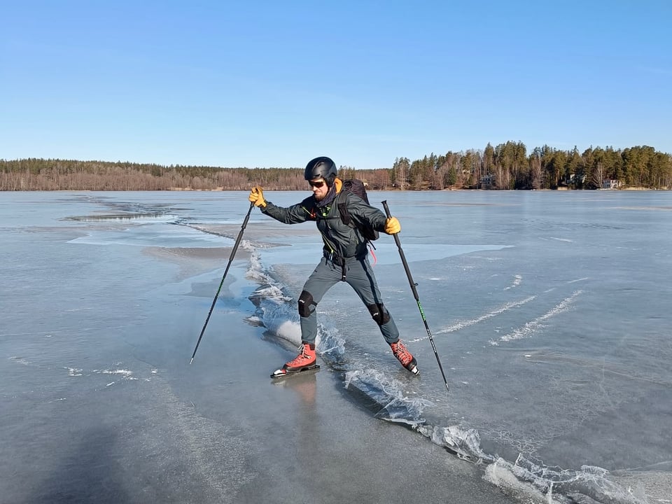 A skater stepping over a rift in the lake ice. It's a sunny day.