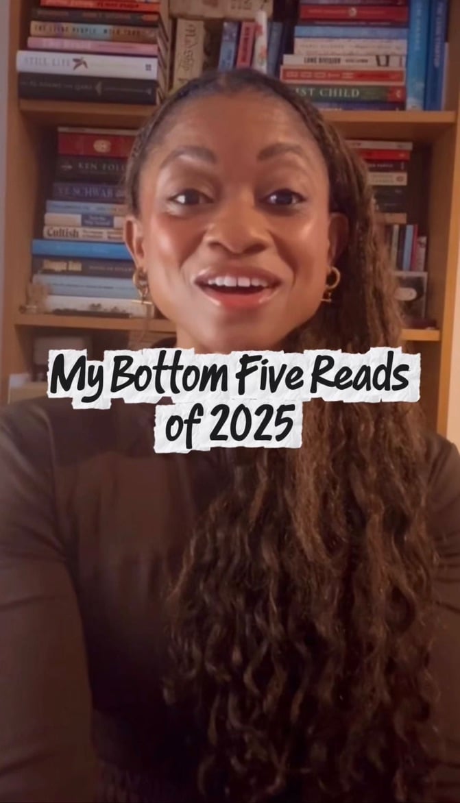 I’m smiling at the camera in front of a wooden bookshelf filled with colorful books. I’m wearing a dark top and gold earrings, and over the image is the text: “My Bottom Five Reads of 2025.”