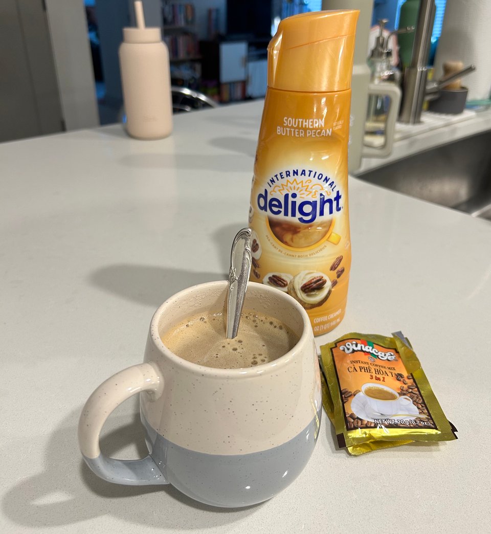 grey and white mug of coffee, with butter pecan creamer and ca phe hoa ta instant vietnamese coffee packet beside it