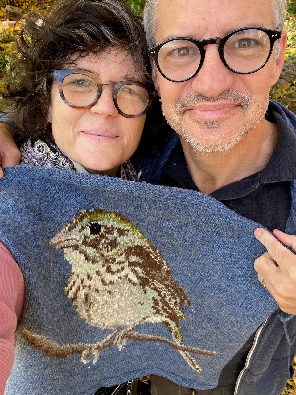 A woman and a man are holding a panel of knitting. The knitting features a Henslow's Sparrow.
