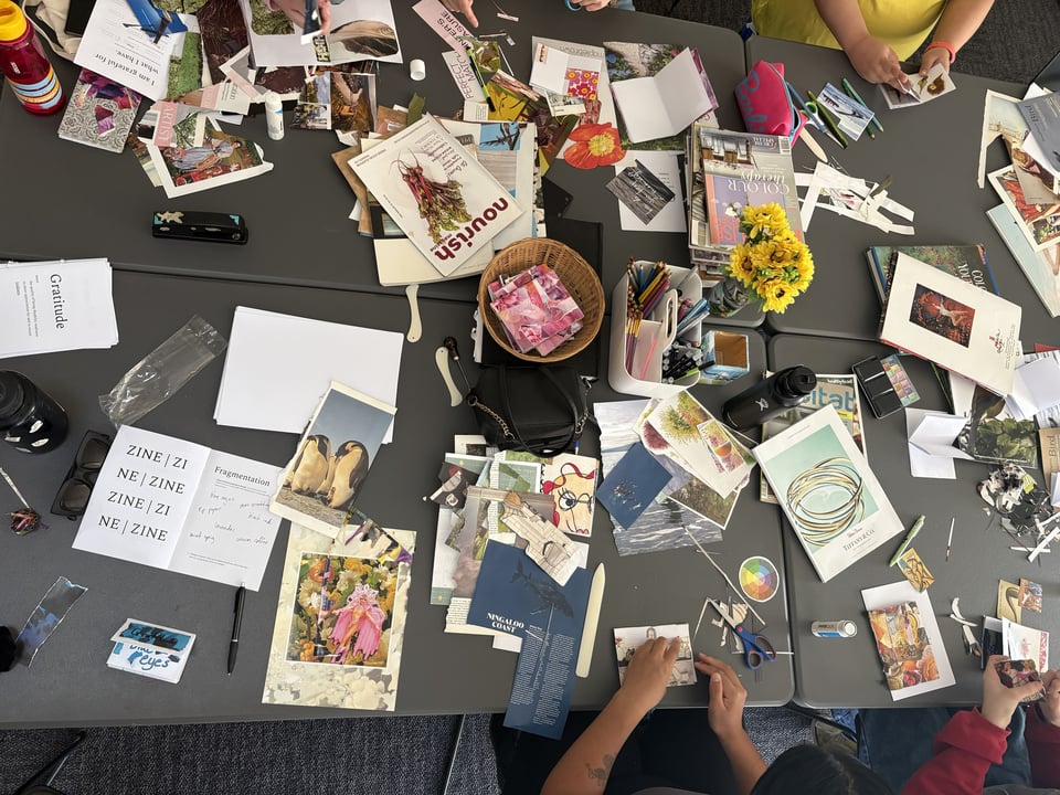 Bird's eye shot of a table of craft - anonymous participant arms and hands working on zines visible.