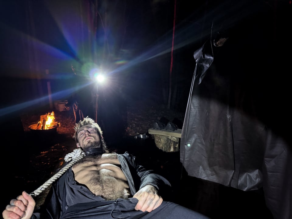 a man in a jumpsuit bares his chest outside at night