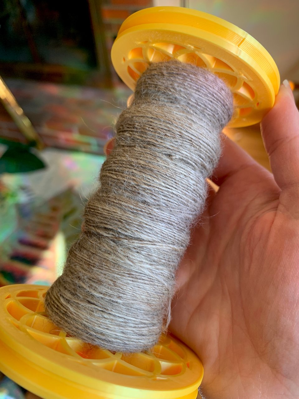 A bobbin full of sandy-colored handspun wool thread. 