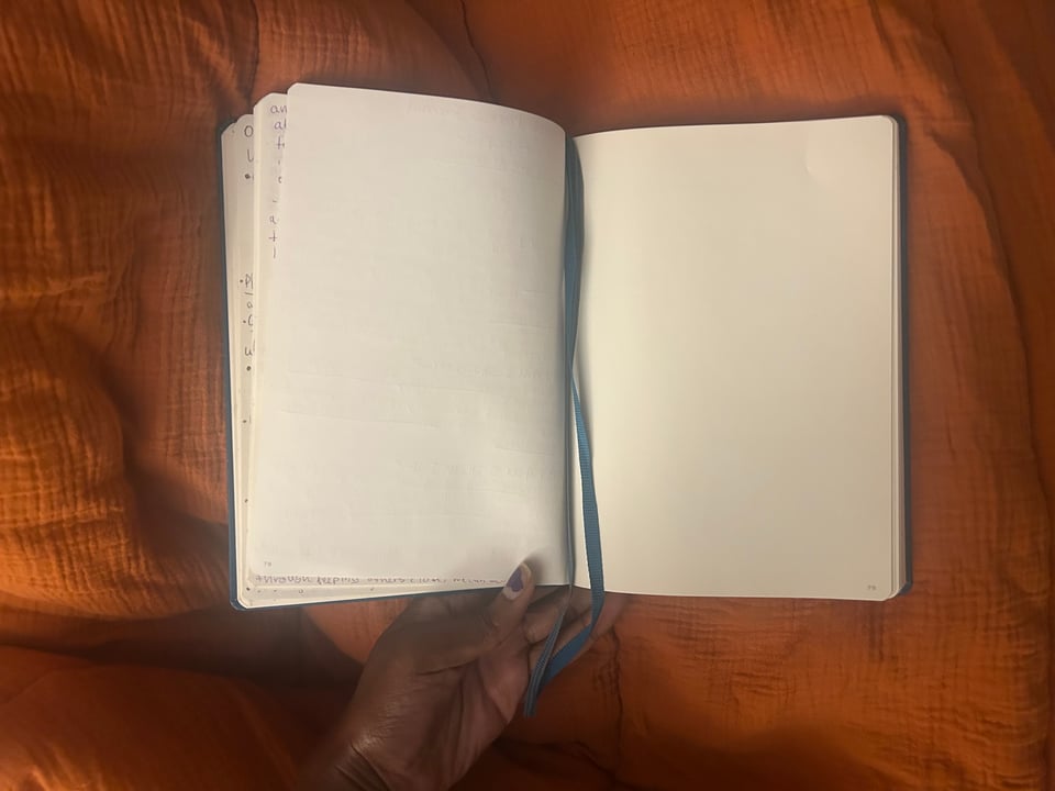 An open notebook with blank pages and a blue ribbon bookmark, resting on an orange textured surface.