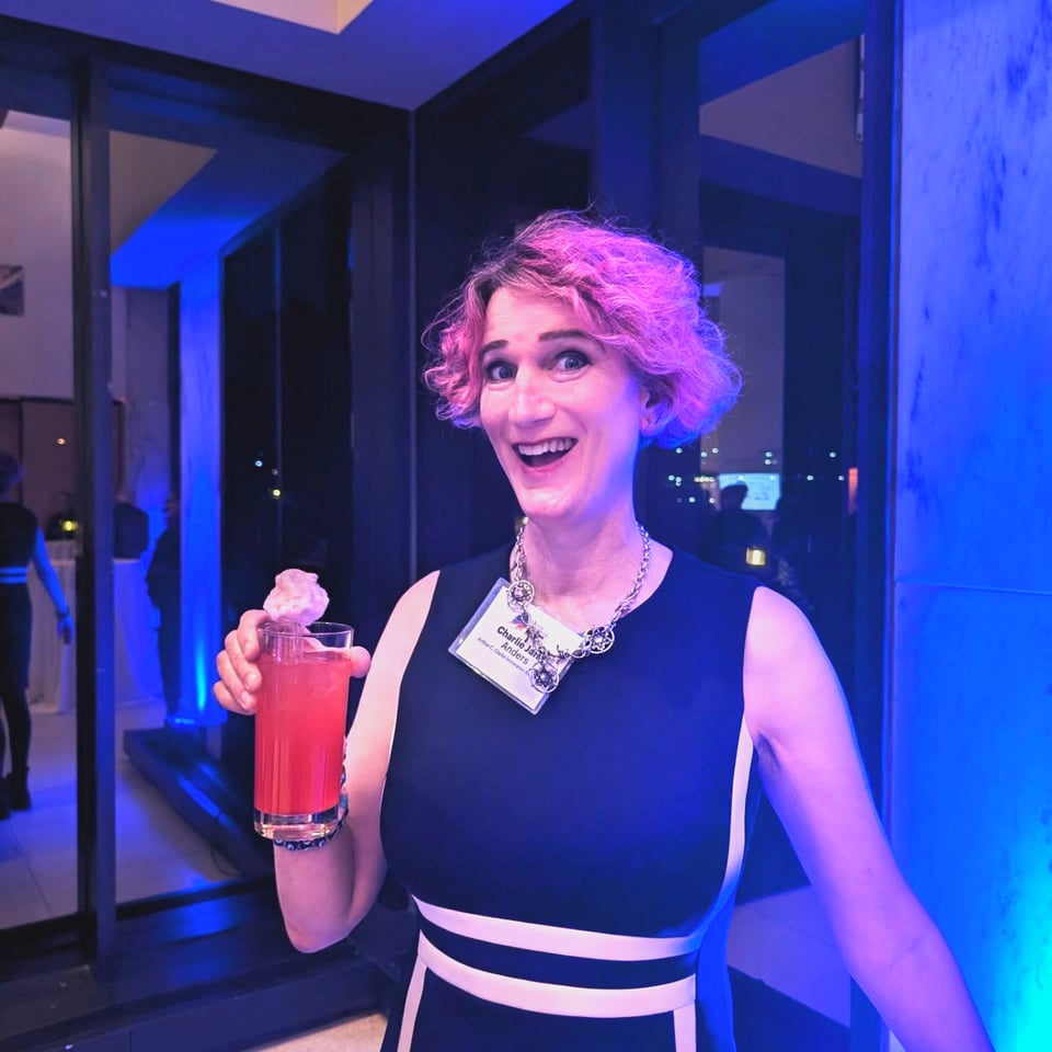 Trans woman with pink hair wearing a a black dress with white stripes holding a pink drink with pink cotton candy on top