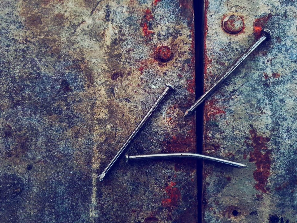 Three metal nails, one of which is bent, on a rusty surface. Photo by Varshil Changani on Unsplash