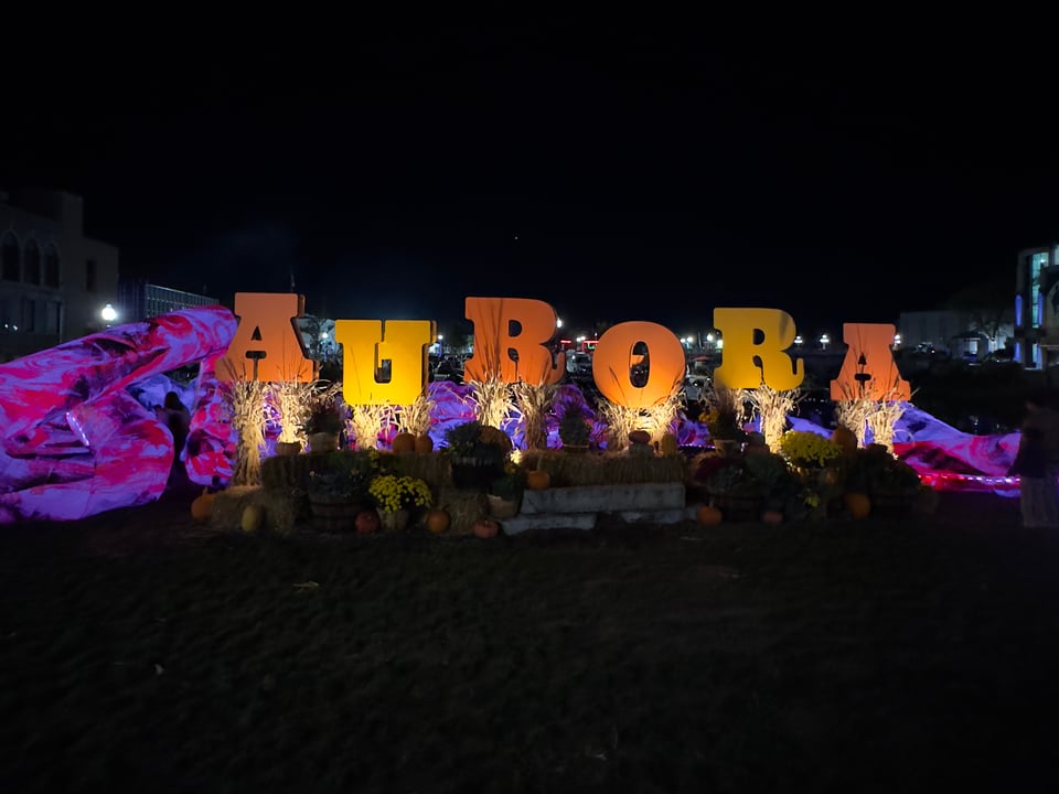 Night photo of orange and yellow Aurora sign on hay bales.