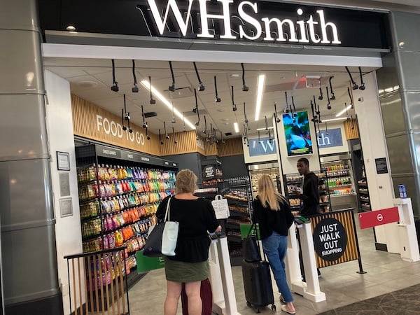 WHSmith store showing customers walking in via entrance gates past a "JUST WALK OUT" sign.