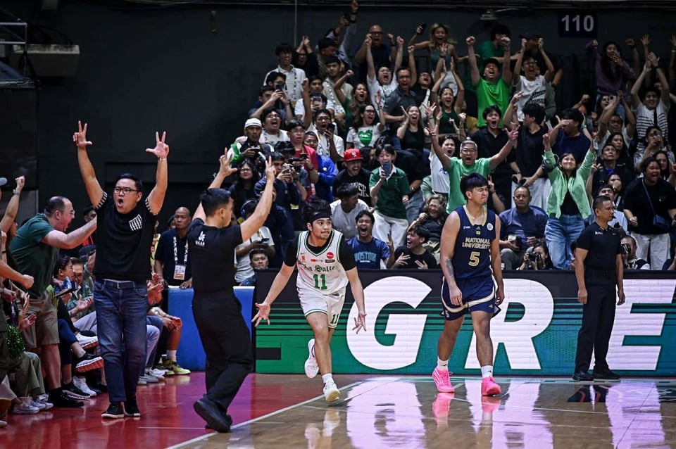 a filipino baller in motion, his fingers in a three-point hand sign, while the crowd celebrates behind him