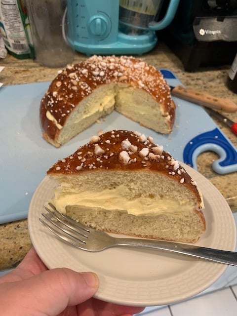 A piece of tarte tropezienne, which is a round piece of broiche with cream sandwiched in between, sits on a white plate with a fork