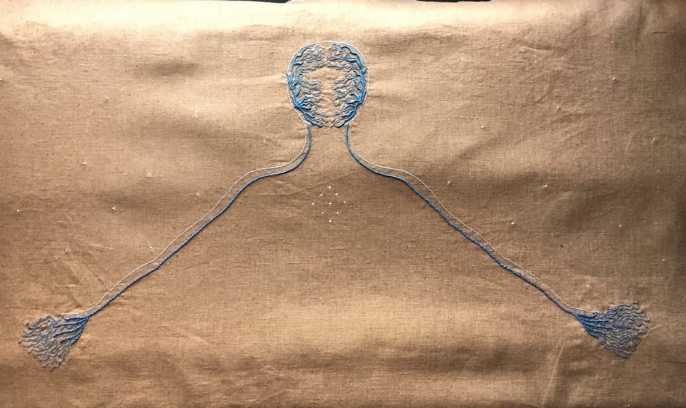 Stars Within, Stars Without by Lia Pas. Tan colored fabric with blue embroidery showing an abstracted outline of a person's head, shoulders, arms, and hands. Click image to view source.