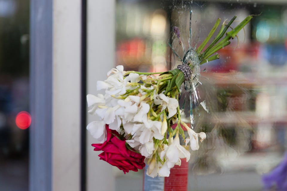 A bouquet of flowers placed in a bullet hole in a glass window
