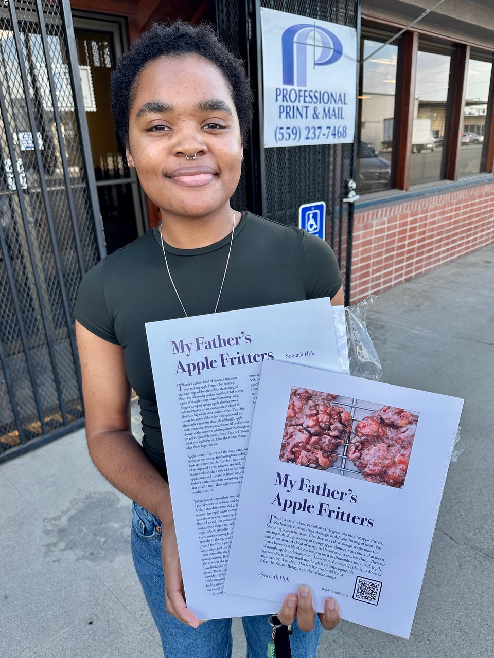 Taylor holds copies of the Soreath Hok broadside in front of Professional Print and Mail offices.