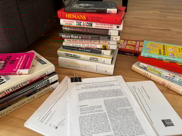 Several stacks of (mostly library) books (plus one DVD) and printouts of journal articles