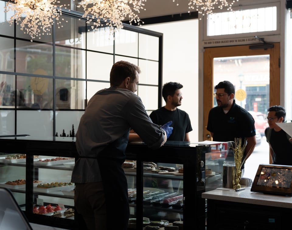 A man who looks mildly like Ryan Gosling in the right light mans a counter of pastries.