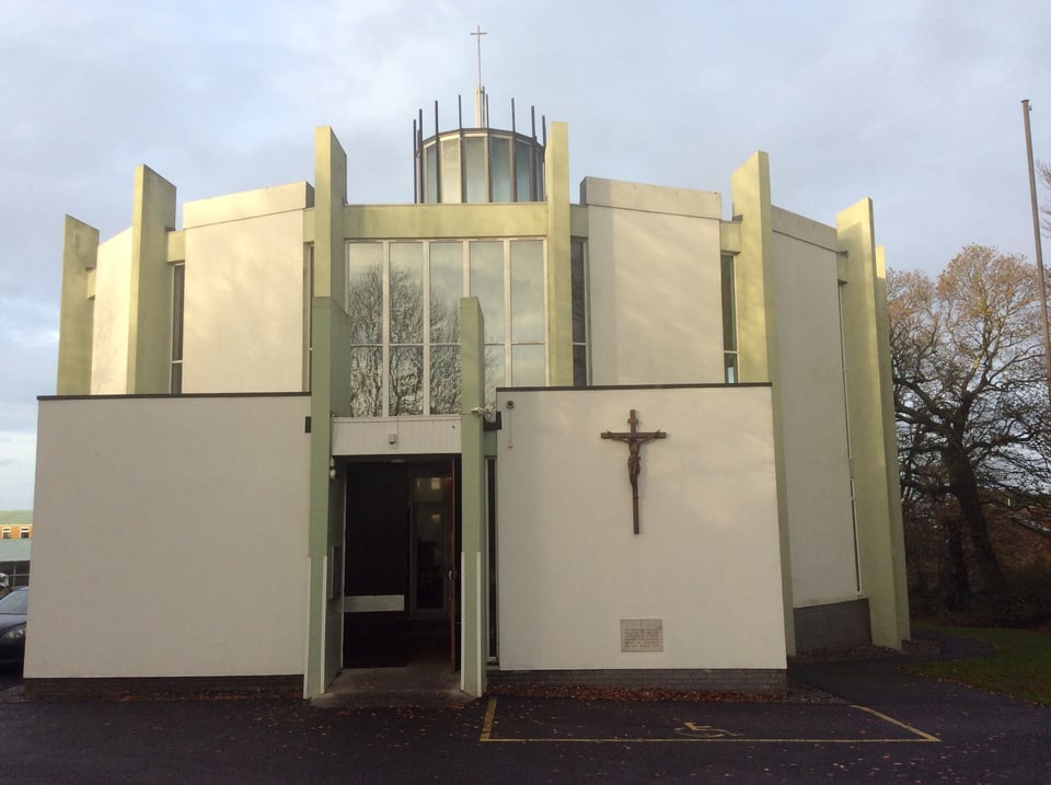 A photo of the church from outside its entrance. The walls are cream and the fins are in a pale green. From this angle, the fins extend into the sky and of the roof only the lantern is visible.