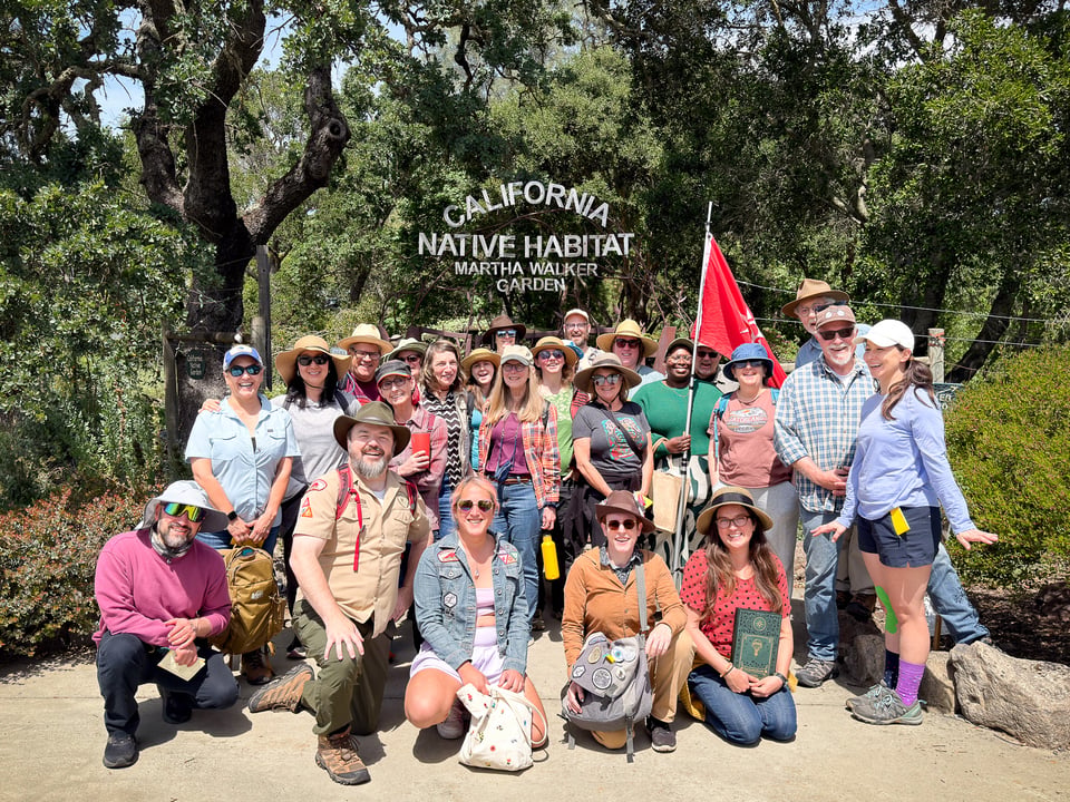 A large group of people, wearing hats and outdoor clothing, poses for a photo in front of the "California Native Habitat" sign at Martha Walker Garden.
