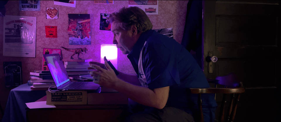 A man films himself on a computer in a cluttered moody room