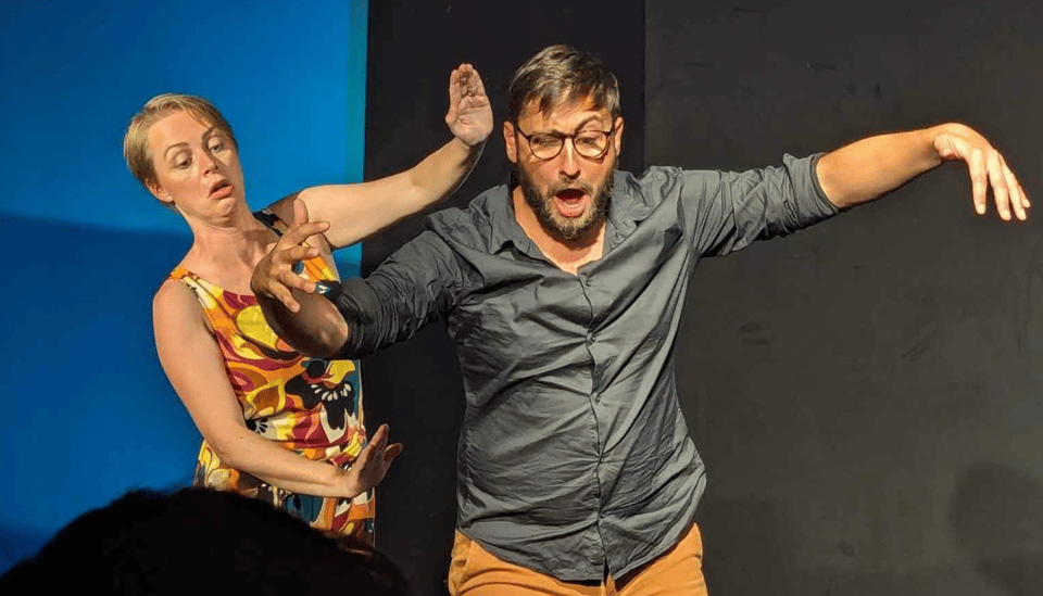 A woman (Laura) and a man (Gael) on stage, making faces
