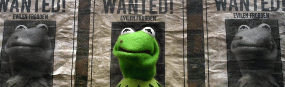 Kermit the Frog sports a black mole and stands in front of a row of wanted posters depicting a frog with a mole. 