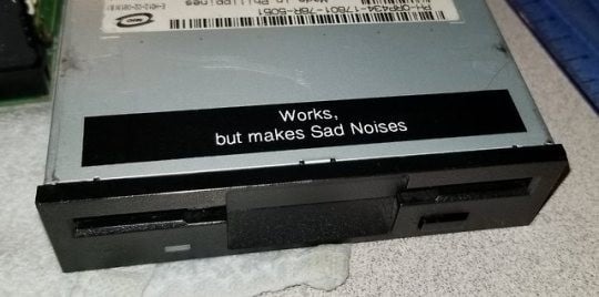 a sata drive with a sticker that says "Works, but makes Sad Noises"