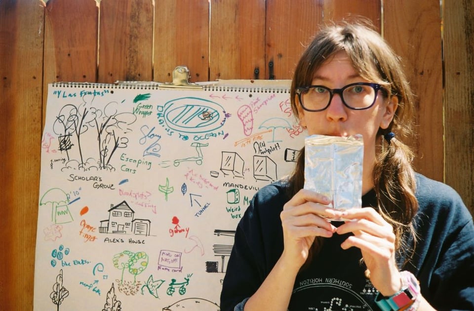 A young woman drinking a juice pouch in front of a childhood drawing