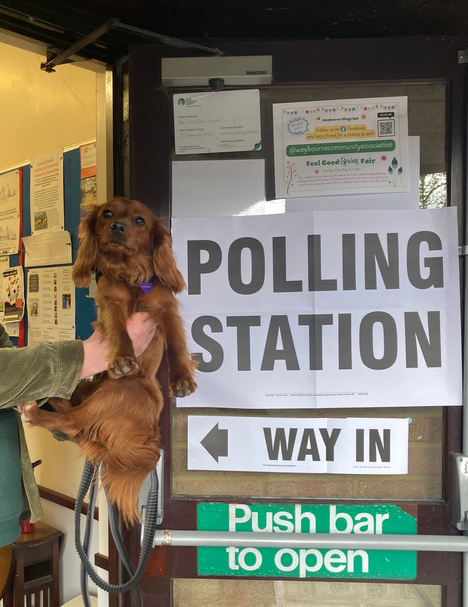 Radio being held up next to a Polling Station sign.