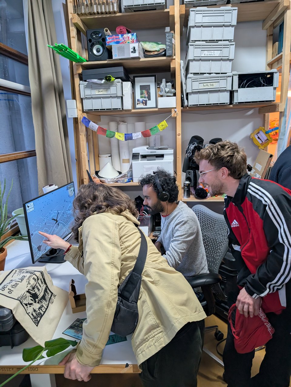 Three people are playing a game that shows a silhouetted pigeon flying over a city. One of the three is pointing excitedly at the screen.