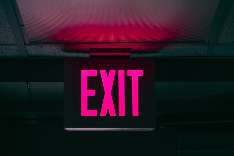 Image is a pink exit sign in a dark hallway