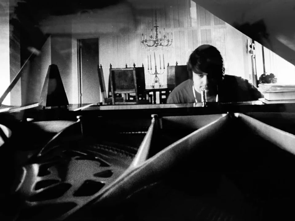 A black and white image of Brian Wilson sitting at a piano.