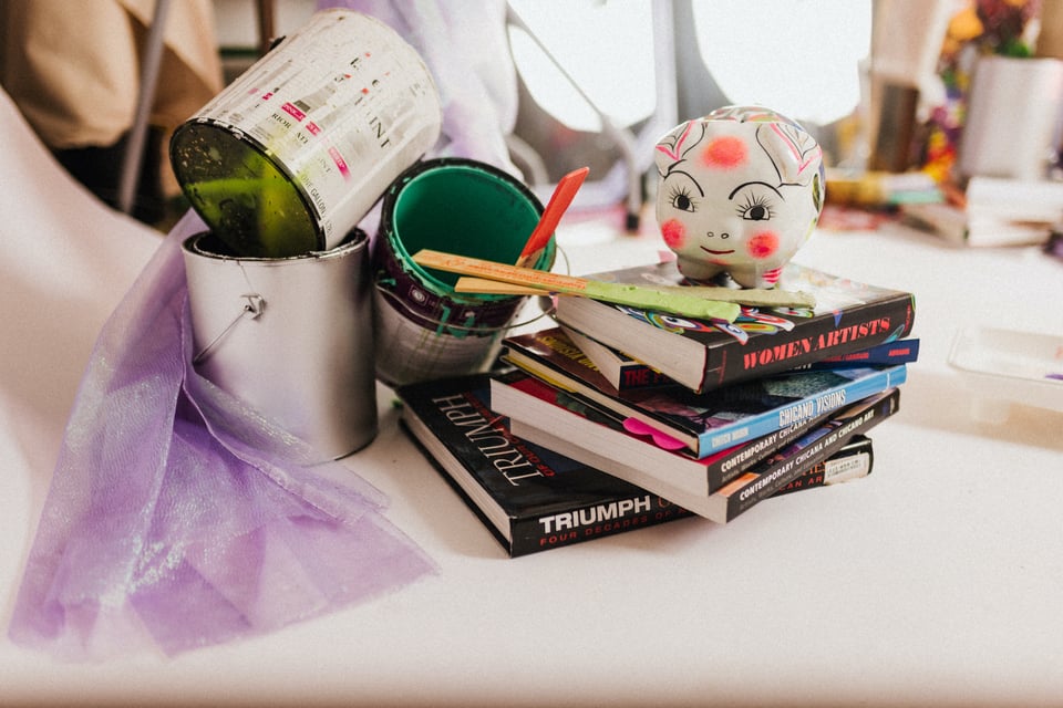 a piggy bank on top of a stack of books with artful paint cans nearby in a chaotic but also staged Studio Utopia scene