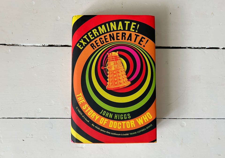 Photograph of a book. The title is "Exterminate! Regenerate!" The subtitle is "The story of Doctor Who" The author is John Higgs. The cover art shows an orange-tinted Dalek overlaid on a multi-coloured vortex spiral pattern.
