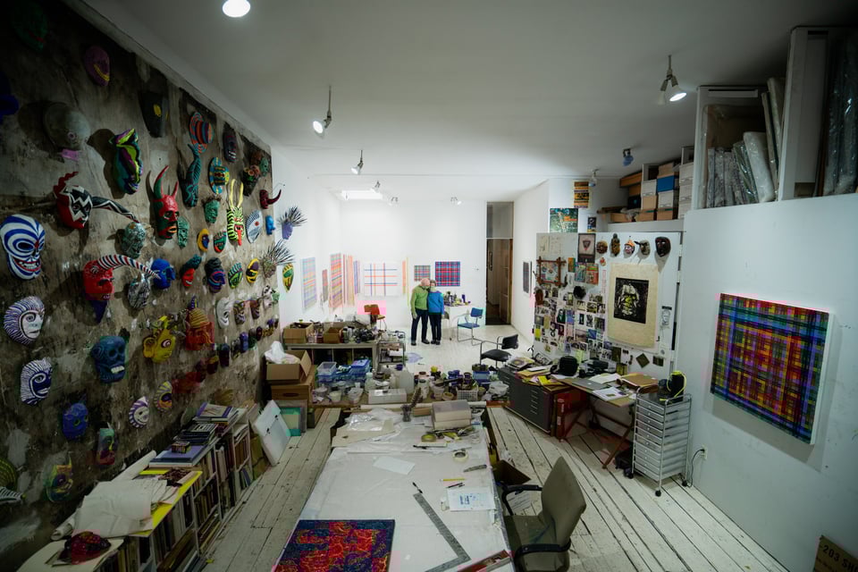 A large studio space captured with a wide lense. The space is filled with art and a couple stands in the distance facing the camera.