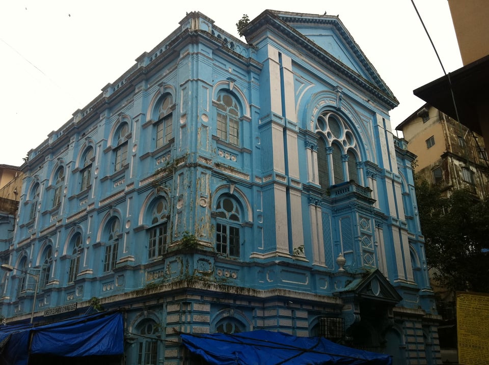 An old building (government? mansion?) painted blue and white cream. It's rotting, seen better days. Has blue construction tarps around its base.