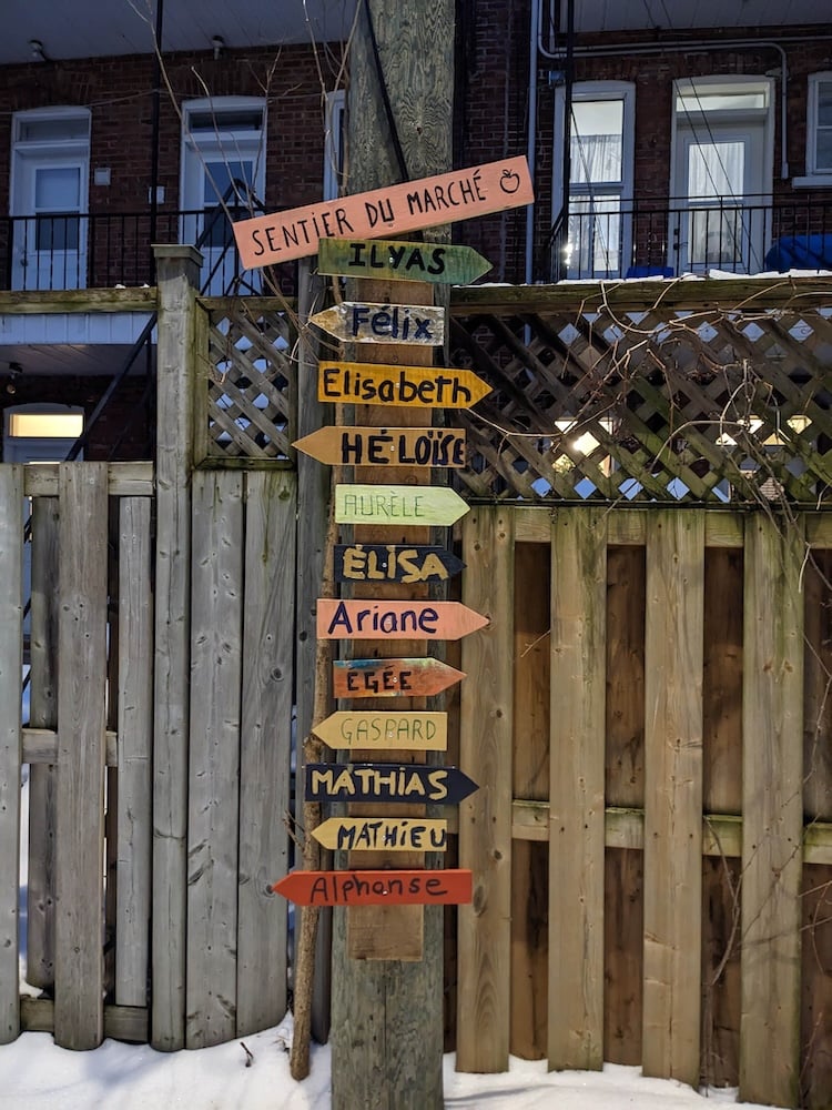 Signs on an electric pole showing the names of children and the direction of their house on a snowy laneway in Montreal