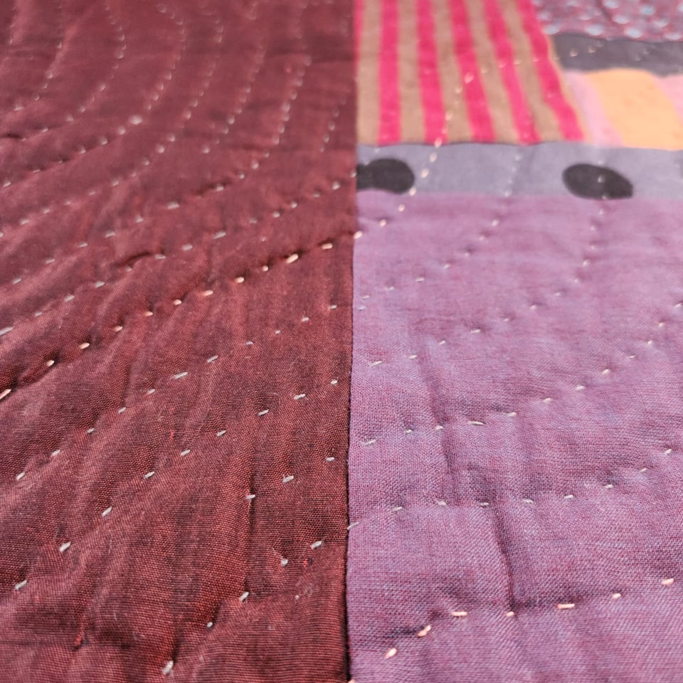 Close up photo of the hand stitching on Concrete Path. Curved lines of stitching are visible against dark purple fabrics.
